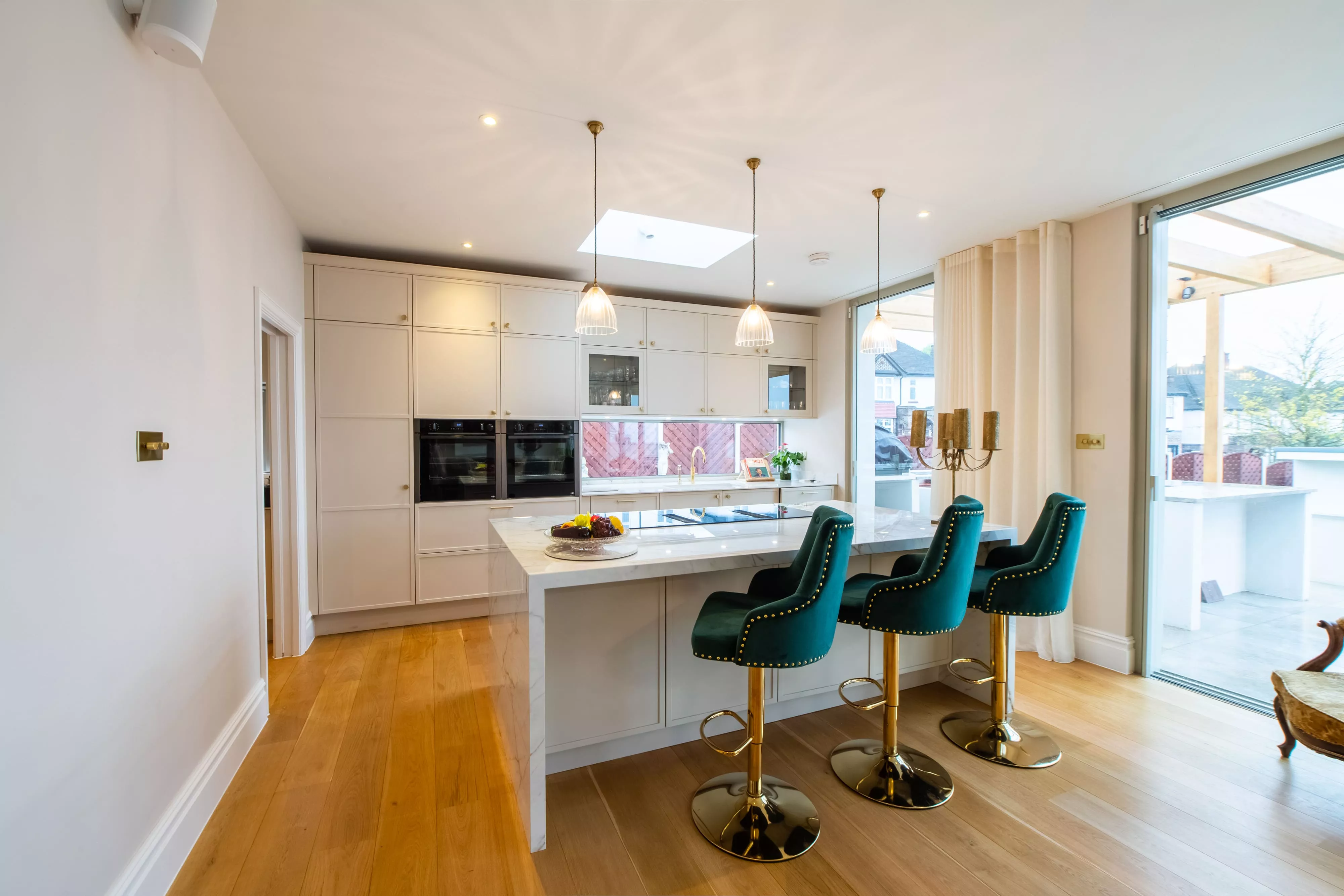 Shaker style kitchen with green material chairs and gold veined marble white worktop